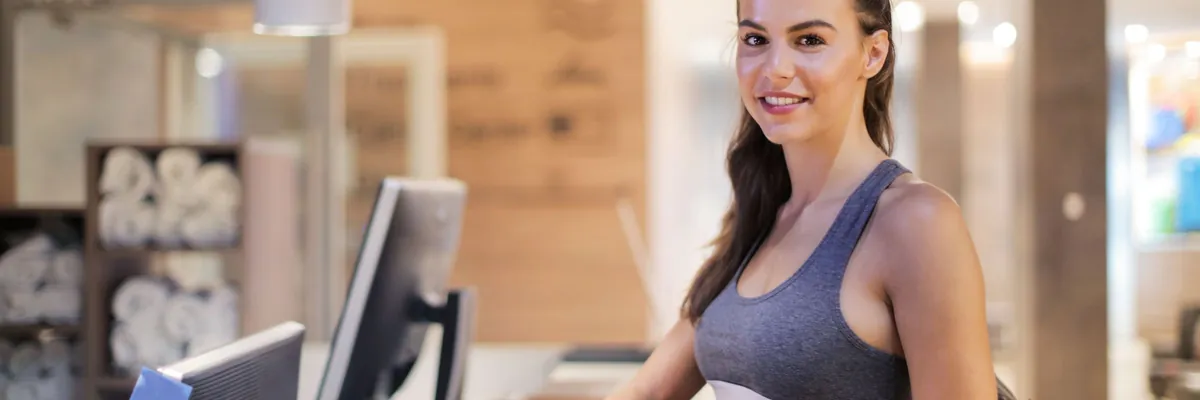 Smiling member in workout clothes at a fitness studio front desk
