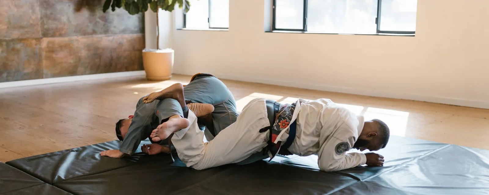 Two jiu-jitsu students grappling on mats in a bright training gym