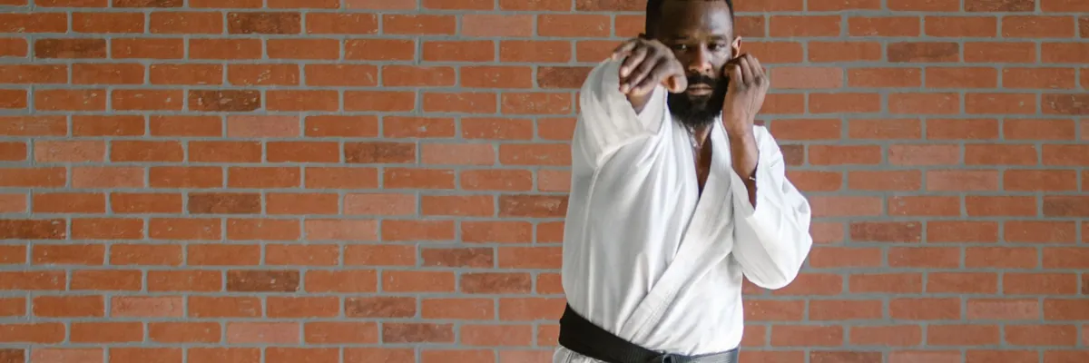 Karate instructor in a white gi and black belt in a brick-walled dojo