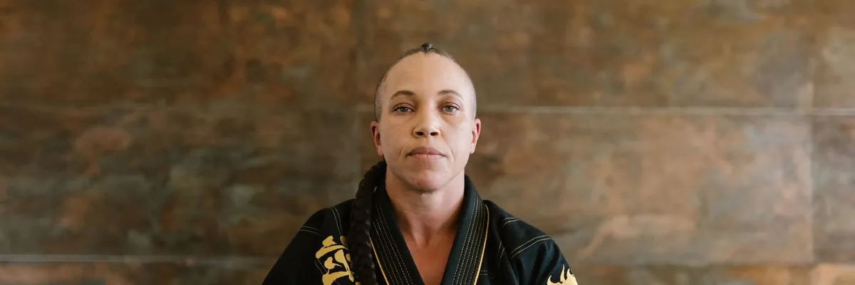Martial artist in a black uniform kneeling on a dojo mat