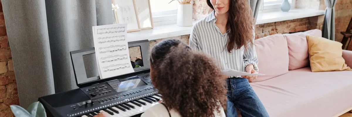 Piano teacher holding sheet music while a student plays a keyboard by the window